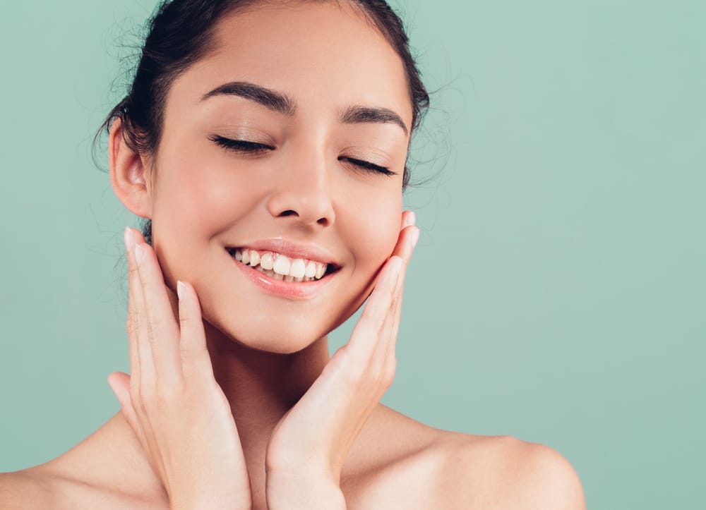 Woman Smiling Peacefully After Urgent Dental Relief – emergency dentist San Diego Young woman with closed eyes smiling softly and touching her cheeks, symbolizing comfort and confidence after emergency dental treatment – emergency dentist San Diego