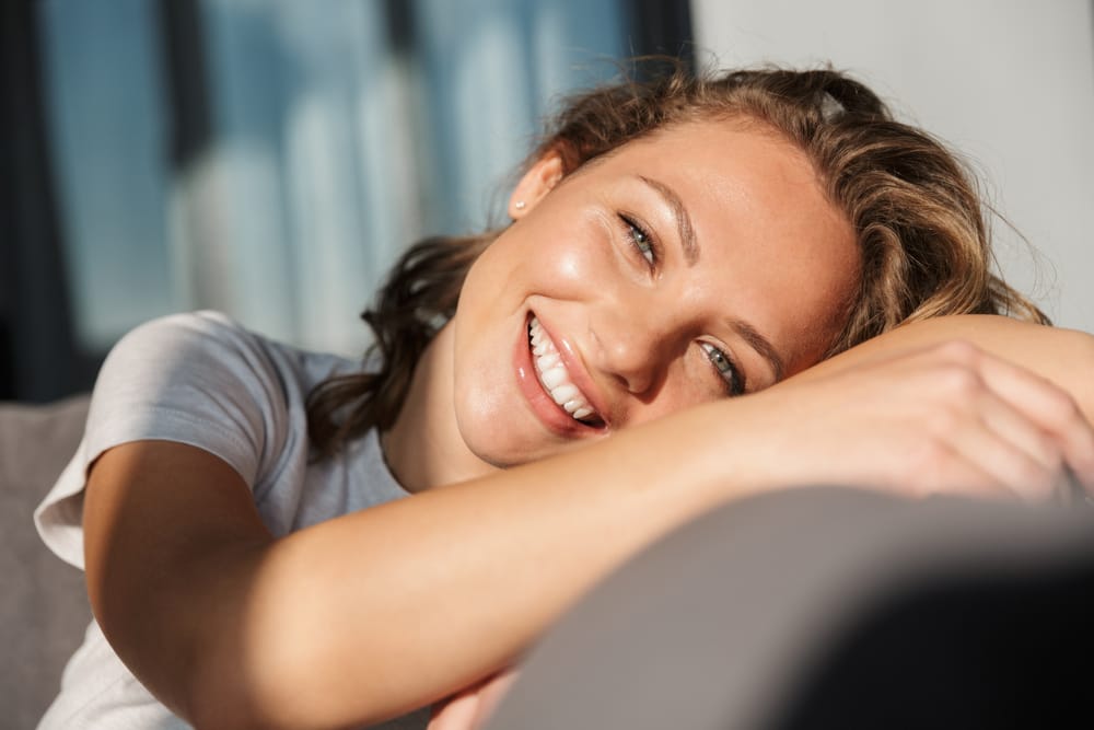 Young woman reclining on a couch and smiling brightly, showcasing healthy, polished teeth after a professional dental visit – dentist San Diego