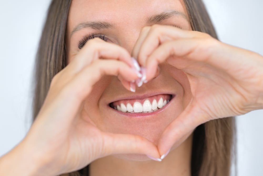 Bright Smile Framed by Hands in Heart Shape – emergency dentist San Diego Smiling woman forming a heart shape with her hands around her teeth, showcasing confidence and gratitude after emergency dental care – emergency dentist San Diego