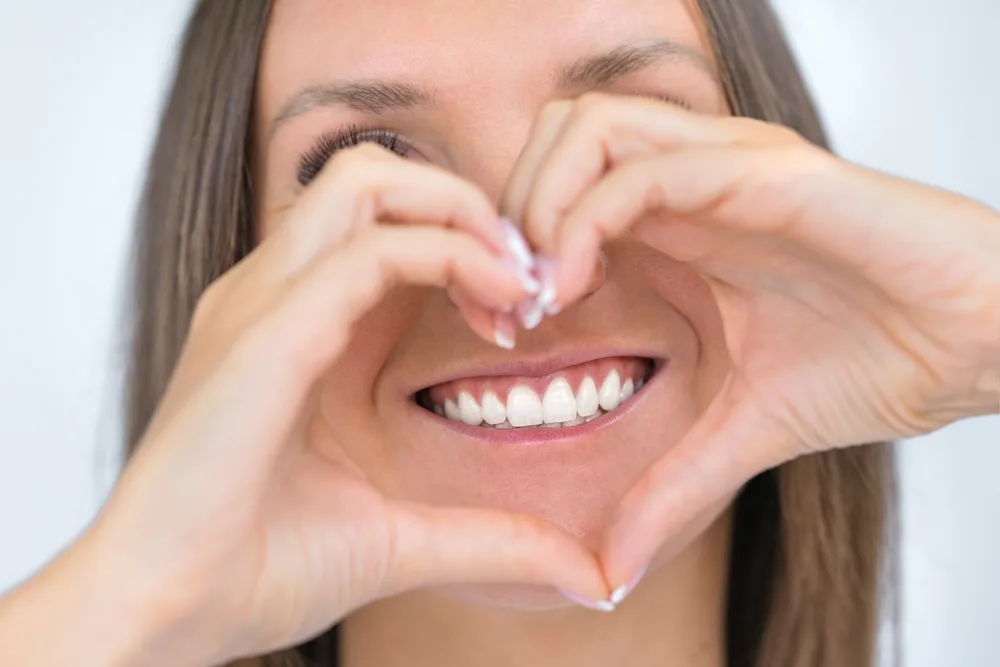 Bright Smile Framed by Hands in Heart Shape – emergency dentist San Diego Smiling woman forming a heart shape with her hands around her teeth, showcasing confidence and gratitude after emergency dental care – emergency dentist San Diego