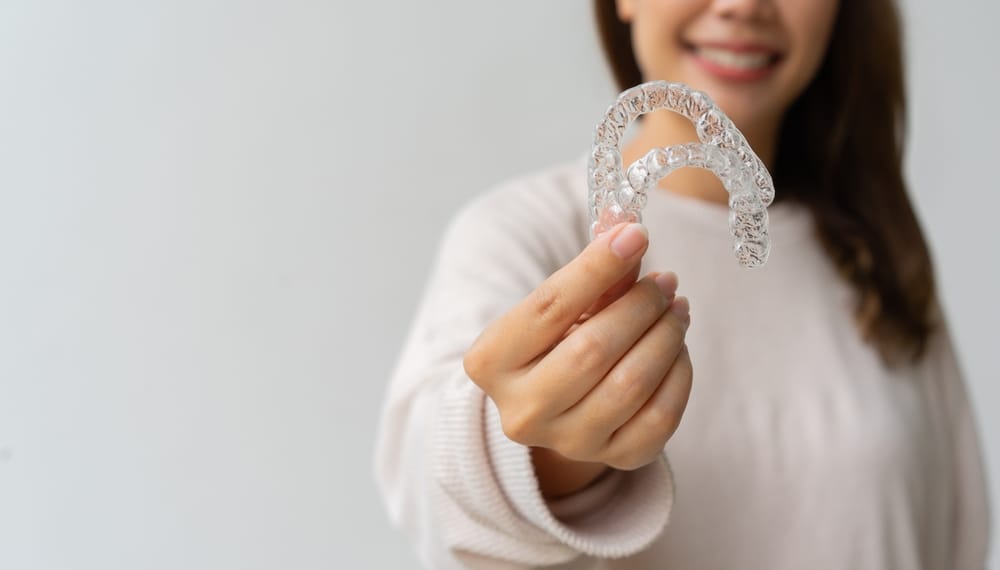 Smiling Woman Holding Invisalign Aligners – emergency dentist San Diego Close-up of a smiling woman holding clear aligners toward the camera, representing urgent orthodontic solutions or retainer repairs – emergency dentist San Diego