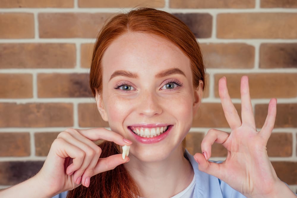 female with snow white smile holding white wisdom tooth - Wisdom Tooth Removal